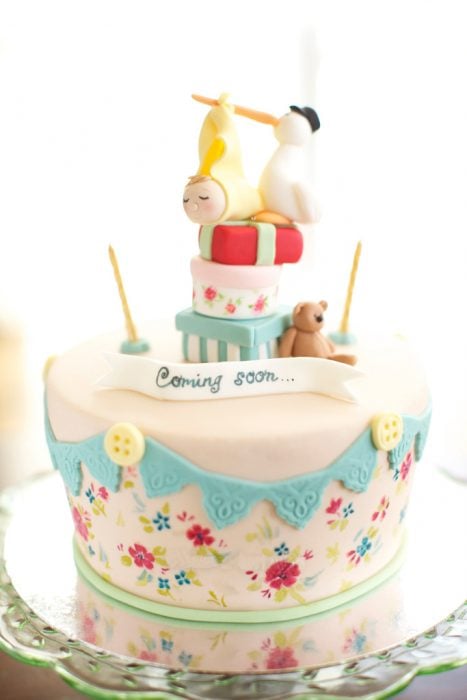 pastel de baby shower con decoraciones de flores y una cigüeña en la parte superior 