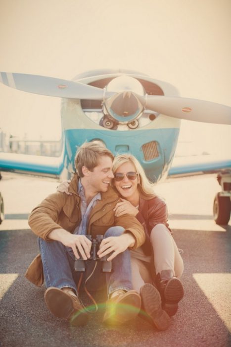 Pareja sentada en la pista de aterrizaje frente a un avión