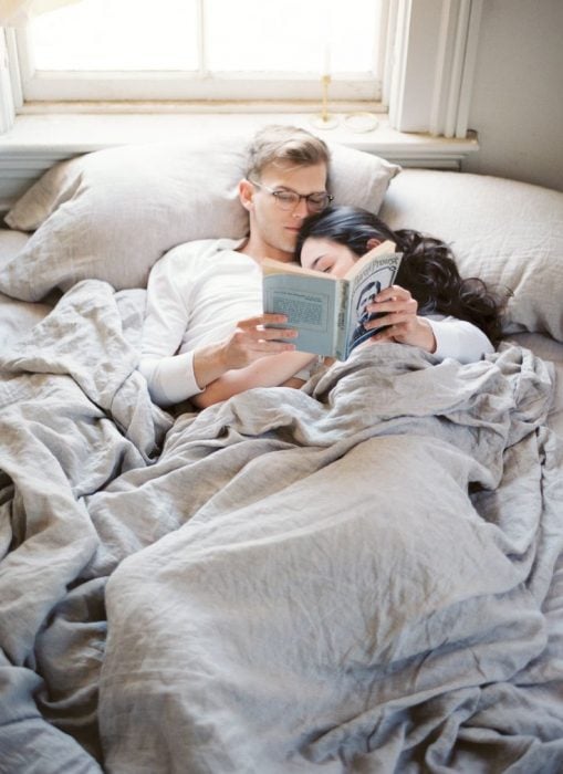 pareja de novios recostados en la cama mientras él le esta leyendo un libro 