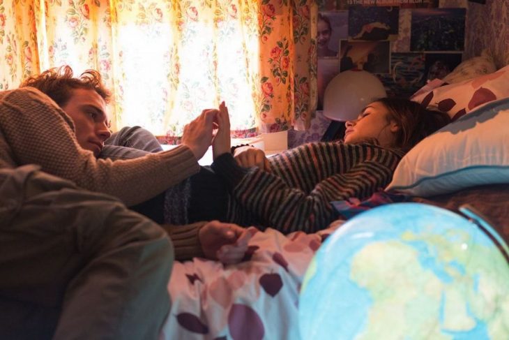 Pareja de novios recostados en la cama frente a una ventana conversando 