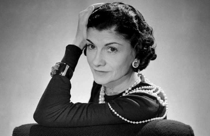 Diseñadora de modas coco chanel sentada y con su brazo recargado sobre su cabeza 