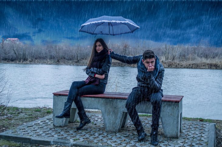 Chica enojada y su novio protegiéndola de la lluvia 