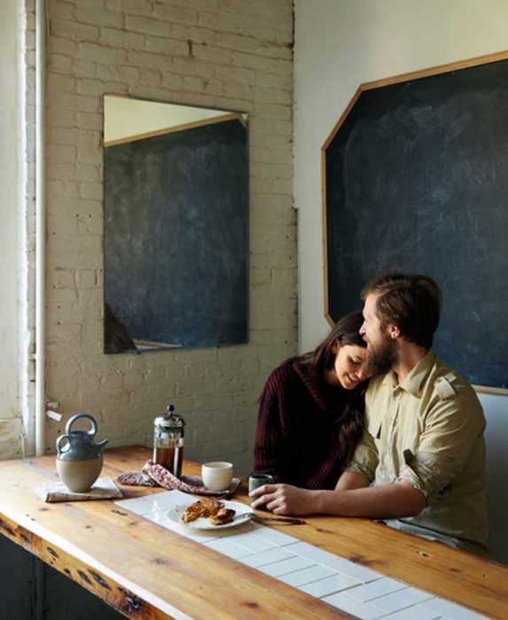 chico con barba abrazando a una chica mientras están en la mesa de la cocina comiendo 