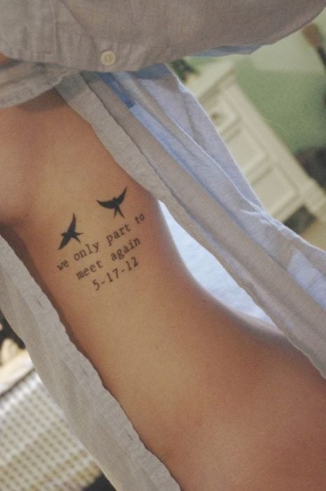 Chica con una blusa color azul mostrando su tatuaje que es una frase con dos pájaros 