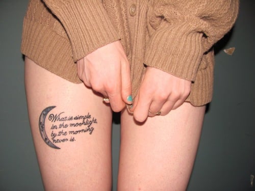chica con una frase tatuada en la pierna usando solo un súeter 