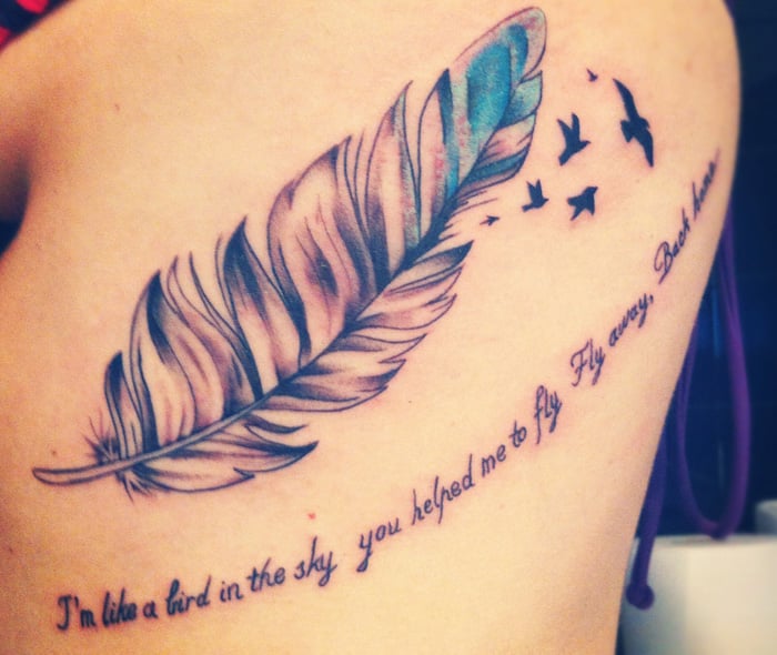 chica con un tatuaje en forma de pluma de ave con una frase sobre su espalda 