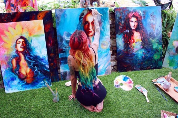 Chica de espaldas pintando un cuadro de una mujer 