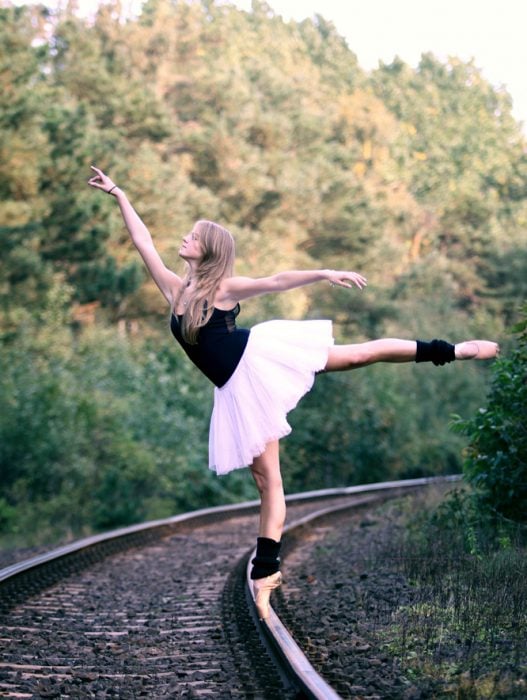 bailarina de ballet parada en puntas sobre las vías del tren 