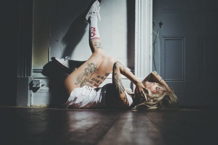 Chica con tatuajes acostada en el suelo 
