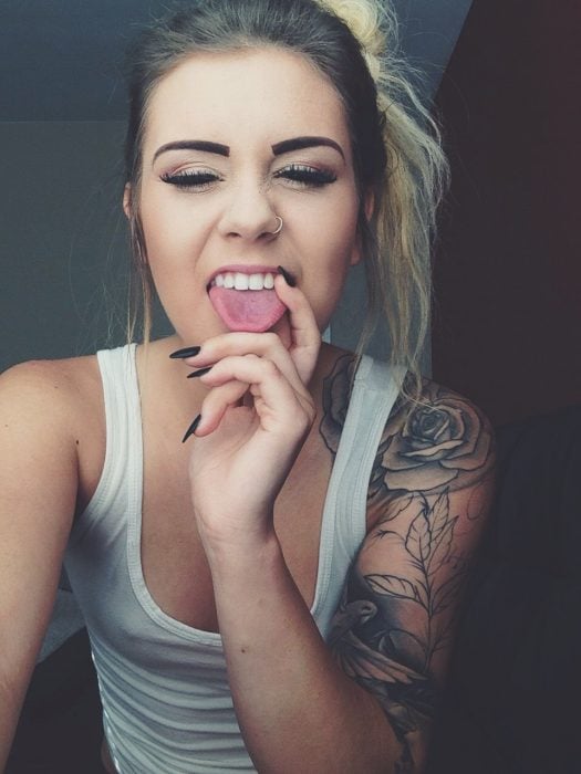 Chica sacando la lengua y con tatuajes en el brazo 