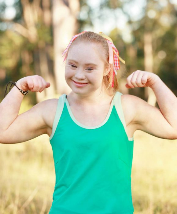 nIÑA CON SÍNDROME DE DOWN LEVANTANDO LOS BRAZOS PARA MOSTRAR SUS MÚSCULOS 