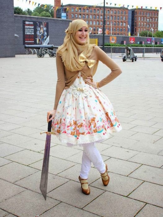 Chica usando un vestido blanco con flores amarillas, mayas y zapatos de color dorado como su suéter y su hijab