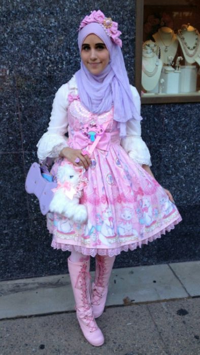 Chica musulmana usando un vestido de color rosa con accesorios y bolsa de conejo y un hijab en la cabeza 