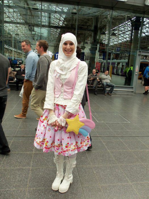 Chica usando un vestido de color ros con flores amarillas y rojas mientras sostiene una bolsa en forma de arcoiris 