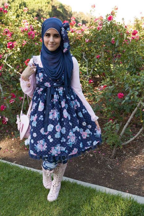 Chica usando un vestido de color azul con flores, suéter rosa y bolsa blanca con un hijab de color azul 