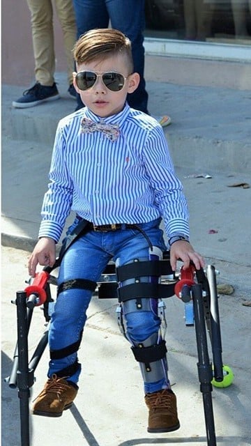 Niño fashionista con discapacidad sentado sobre una silla de ruedas 