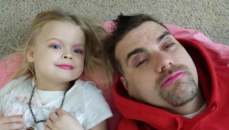 Papá junto a su hija reostados en la alfombra mientras muestran sus maquillajes 