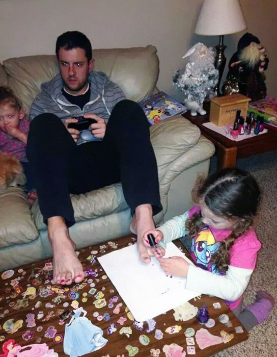 Papá jugando con sus hijas mientras una de ellas le pinta las uñas de los pies 