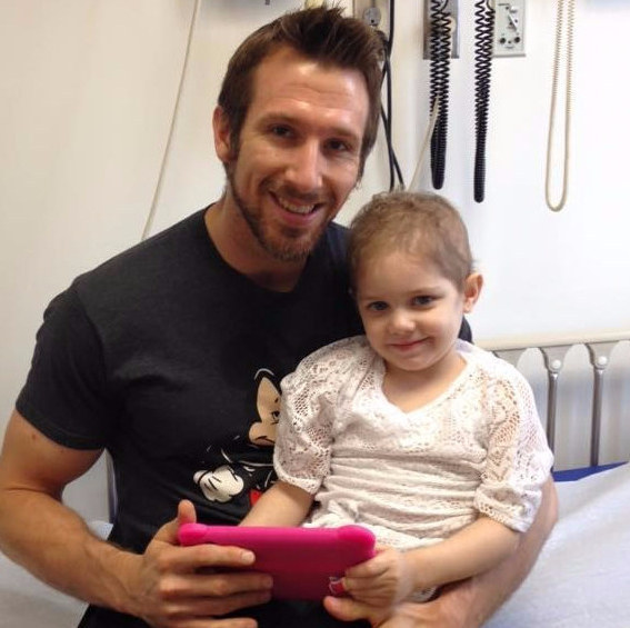 Enfermero sosteniendo a un niña enferma de cáncer mientras ven una tablet 