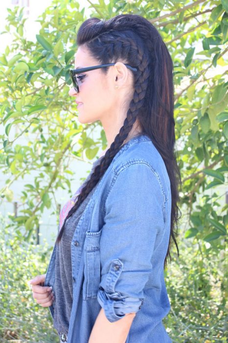 Chica de cabello negro con una trenza de lado, usando una chamarra de mezclilla blusa gris y lentes negros 