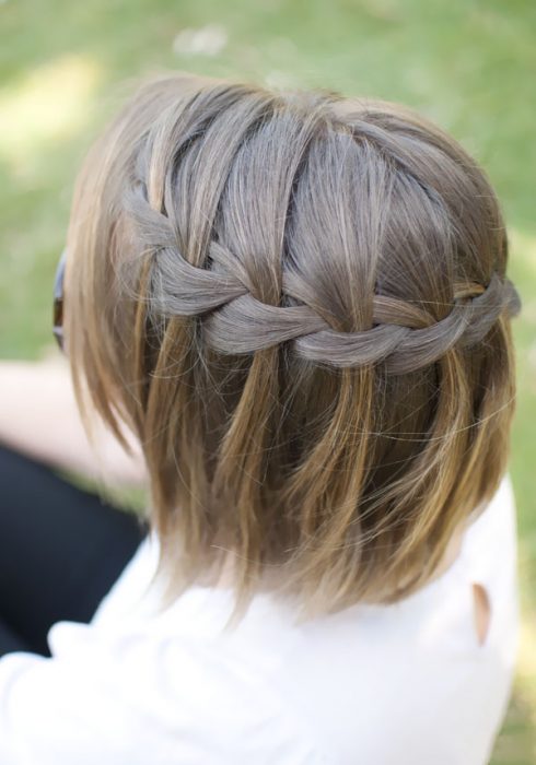 Chica con el cabello corto luciendo una trenza mientras esta de espaldas 