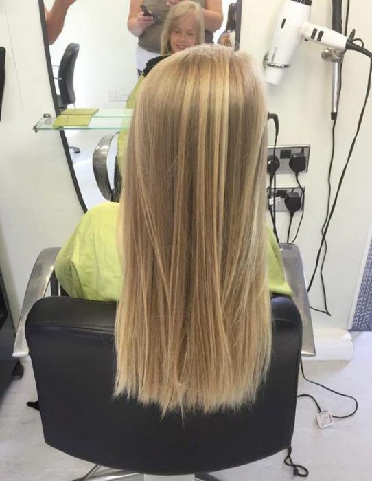 Niña con el cabello largo y rubio sentada en una silla esperando que su estilista corte su cabello 