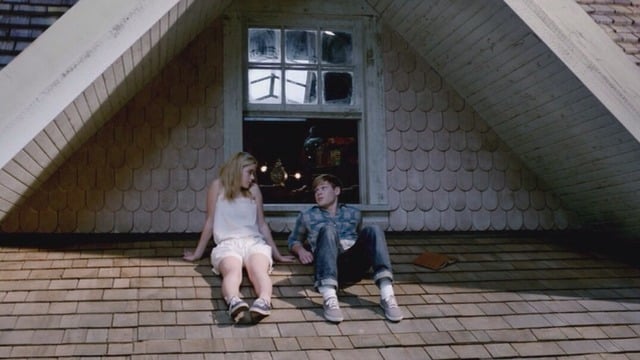 Chico y chica sentados en el tejado de una casa hablando 