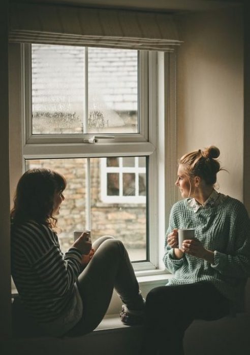 Amigas sentadas frente a una ventana conversando y bebiendo café