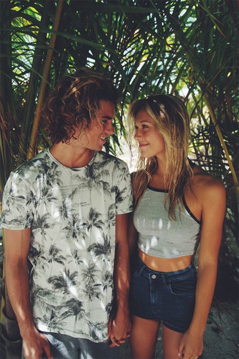 Pareja de novios parados bajo una palmera mientras se están viendo de frente 