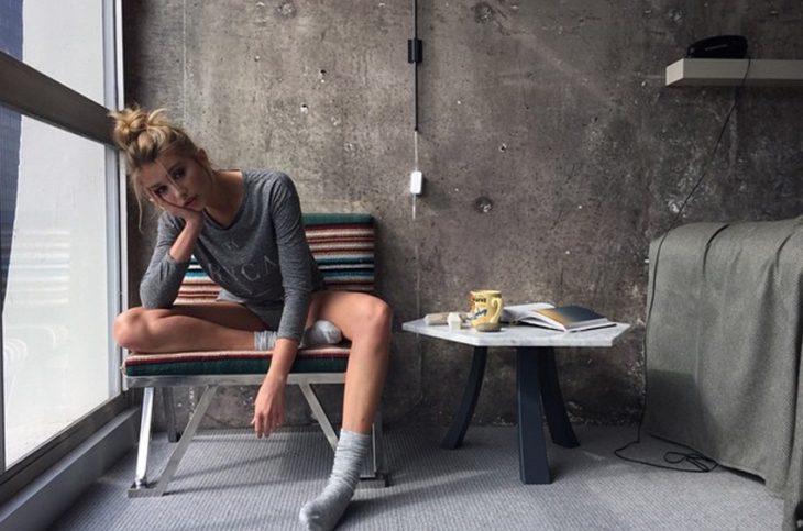 Chica sentada en un sofá pensando mientras usa calcetines y una blusa color gris 