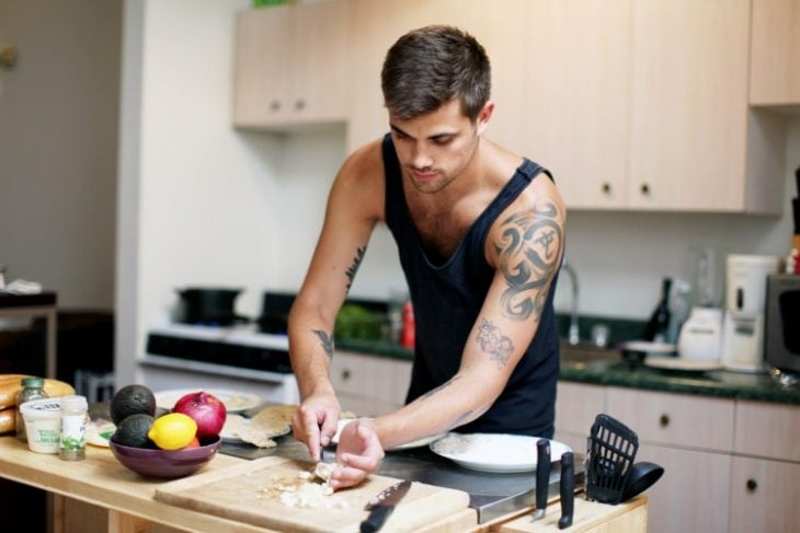 Chico cocinando en una cocina mientras pica verduras sobre una tabla 