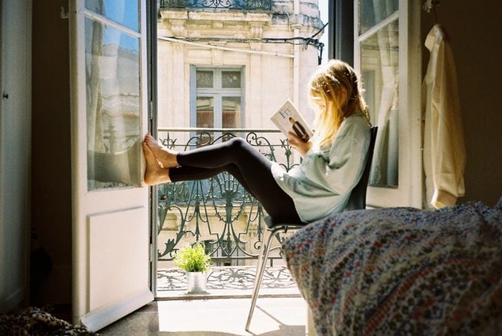 Chica leyendo un libro mientras está sentada en la ventana 
