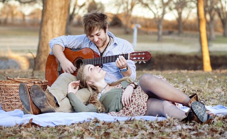 Chico con una guitarra mientras esta recostado en el pasto con una chica 