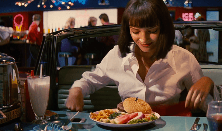 Escena de la película pulp fiction chica sentada comiendo hamburguesa