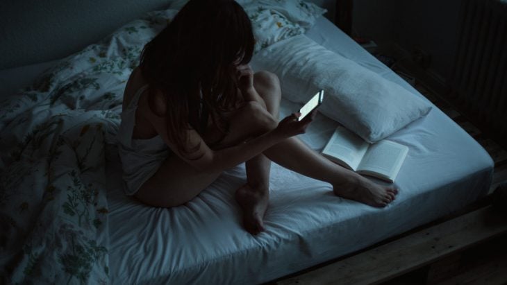 Chica en la cama con un celular 
