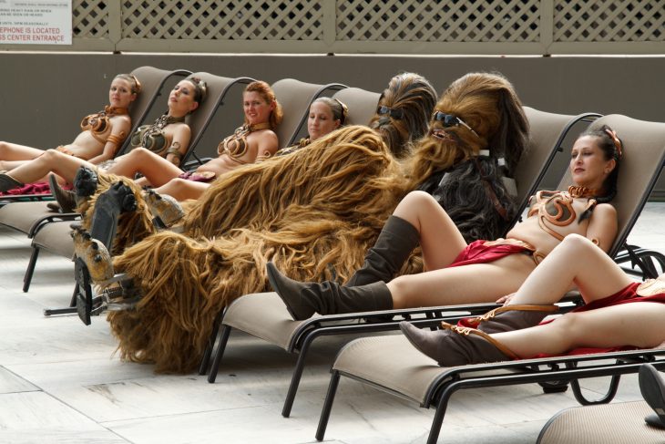 Chicas recostadas en la piscina tomando el sol junto a un hombre vestido de chewacca