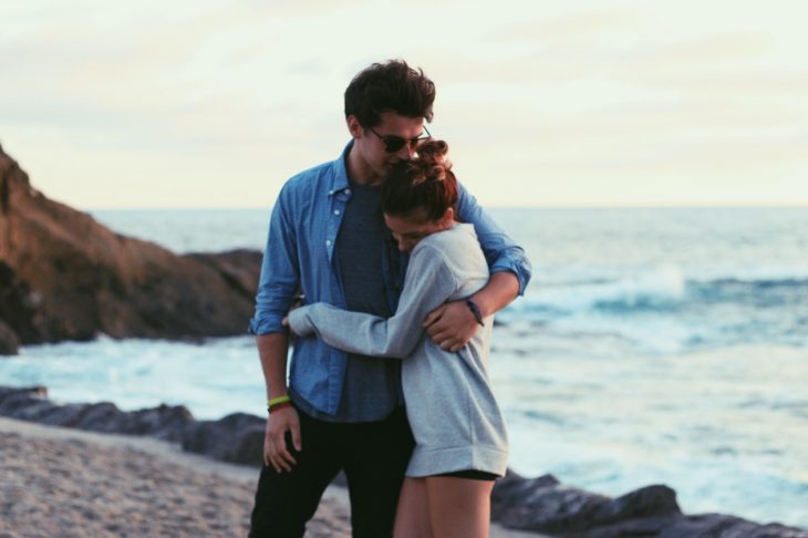 Pareja de novios abrazados mientras están frente al mar 