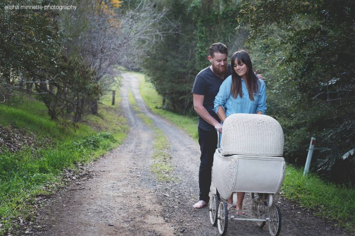 Pareja de novios parados sobre un camino de tierra empujando el coche de un bebé