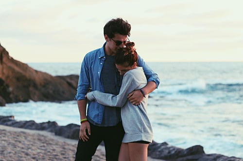 Pareja de novios caminando por la playa abrazados mientras él la besa en la frente 
