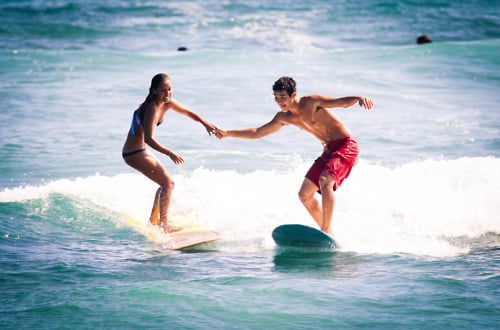 Pareja de novios practicando surf mientras ella lo toma de la mano 