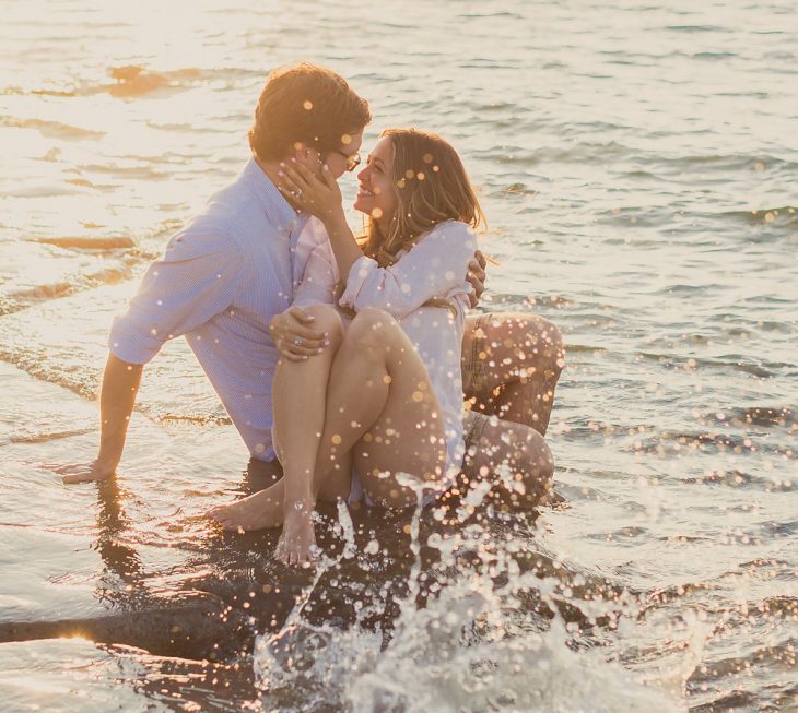 pareja de novios sentaos en la playa mientras los moja una ola 