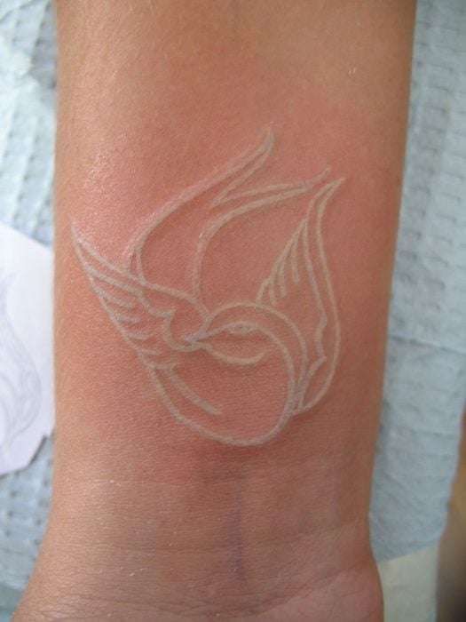 Muñeca de una chica tatuada con un pájaro en tinta blanca 