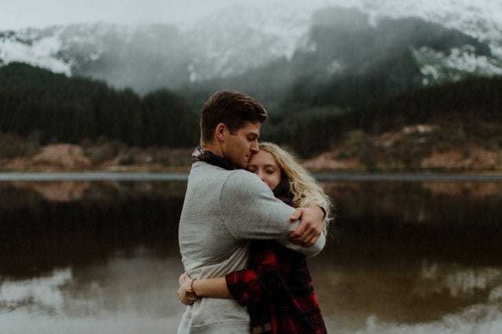 hombre abrazando a un chica mientras estan frente a un lago en invierno