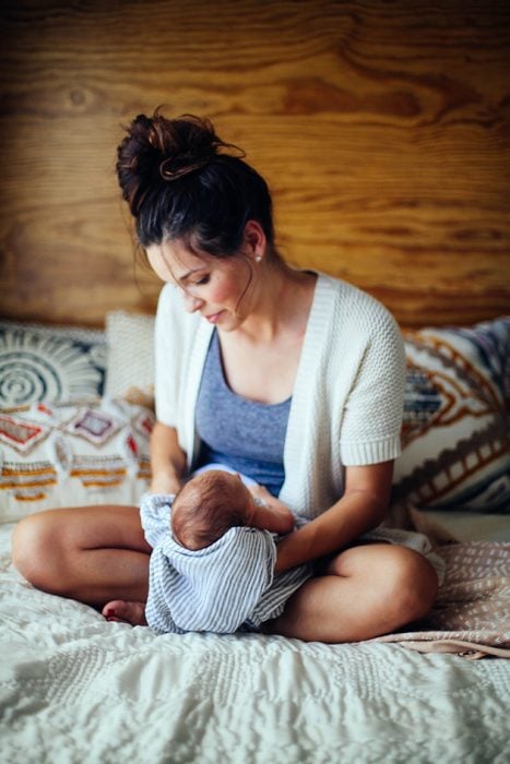 Mujer observando a su bebé meintras está dormido entre sus brazos 