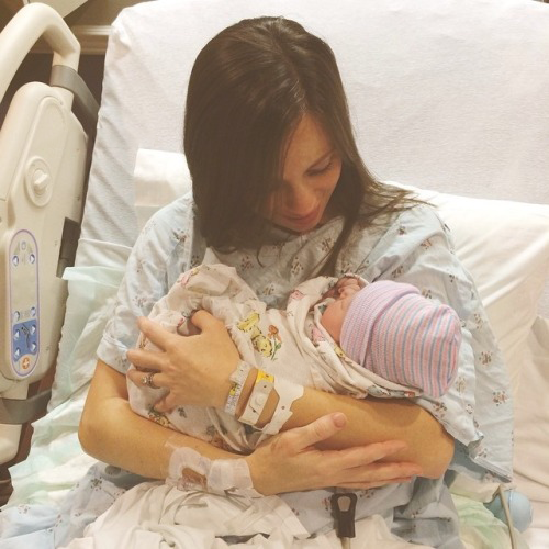 Madre sosteniendo a su bebé en brazos mientras está recostada en la cama de un hospital