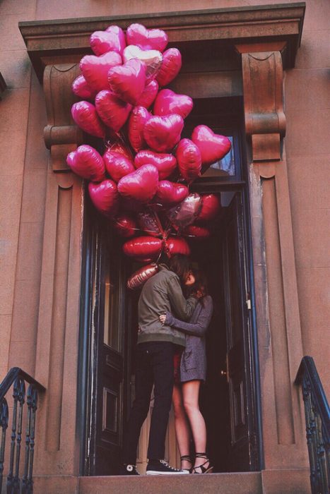 Chico con globos de corazón besando a una chica 