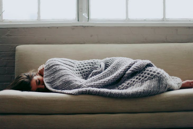 Chica recostada en un sofá tapada con una manta