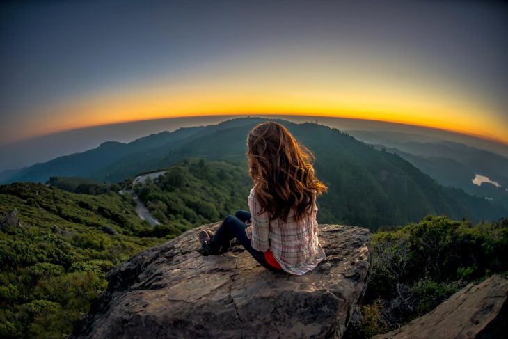 Chica observando un atardecer en una montaña 