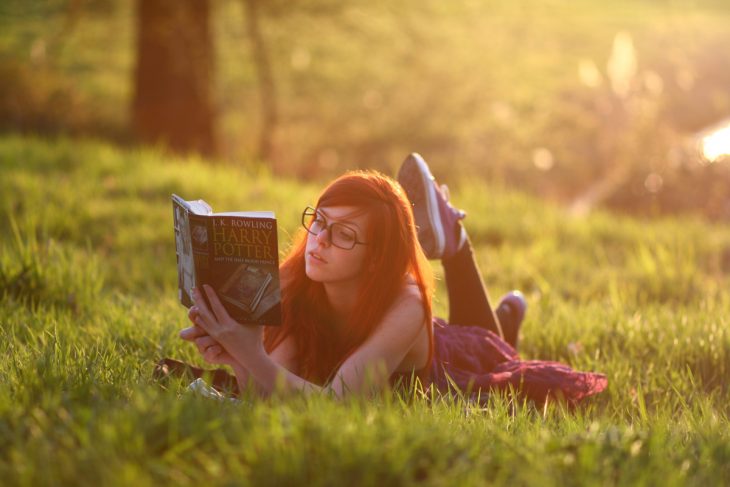 Chica recostada en el pasto leyendo el libro de Harry Potter 