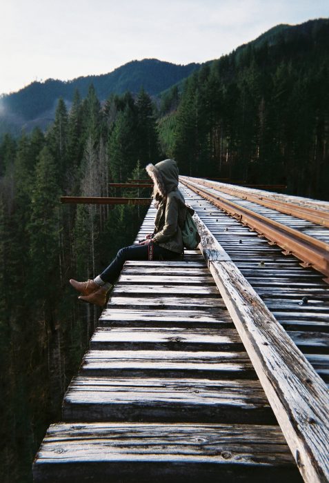 Chica sentada en las vías del tren en medio del bosque 